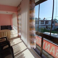 Una habitación con un ventanal grande, una mesa con sillas, un sofá y una cortina estampada.