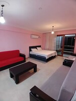 Una habitación de hotel con una cama, un sofá rojo, una mesa de centro negra y un sofá blanco.