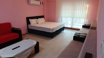 A hotel room with a bed, a red sofa, a white sofa, and a small table.