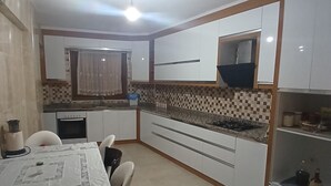 A compact kitchen with white cabinets, a tiled backsplash, a dining table with chairs, and a small refrigerator. - Mehmet Home (Denizli)