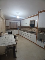 Cocina compacta con armarios blancos, salpicadero de azulejos, una mesa de comedor con sillas y un refrigerador pequeño.