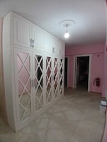 Una habitación con un armario blanco grande con varias puertas y tiradores, una lámpara de techo y una pared rosa.