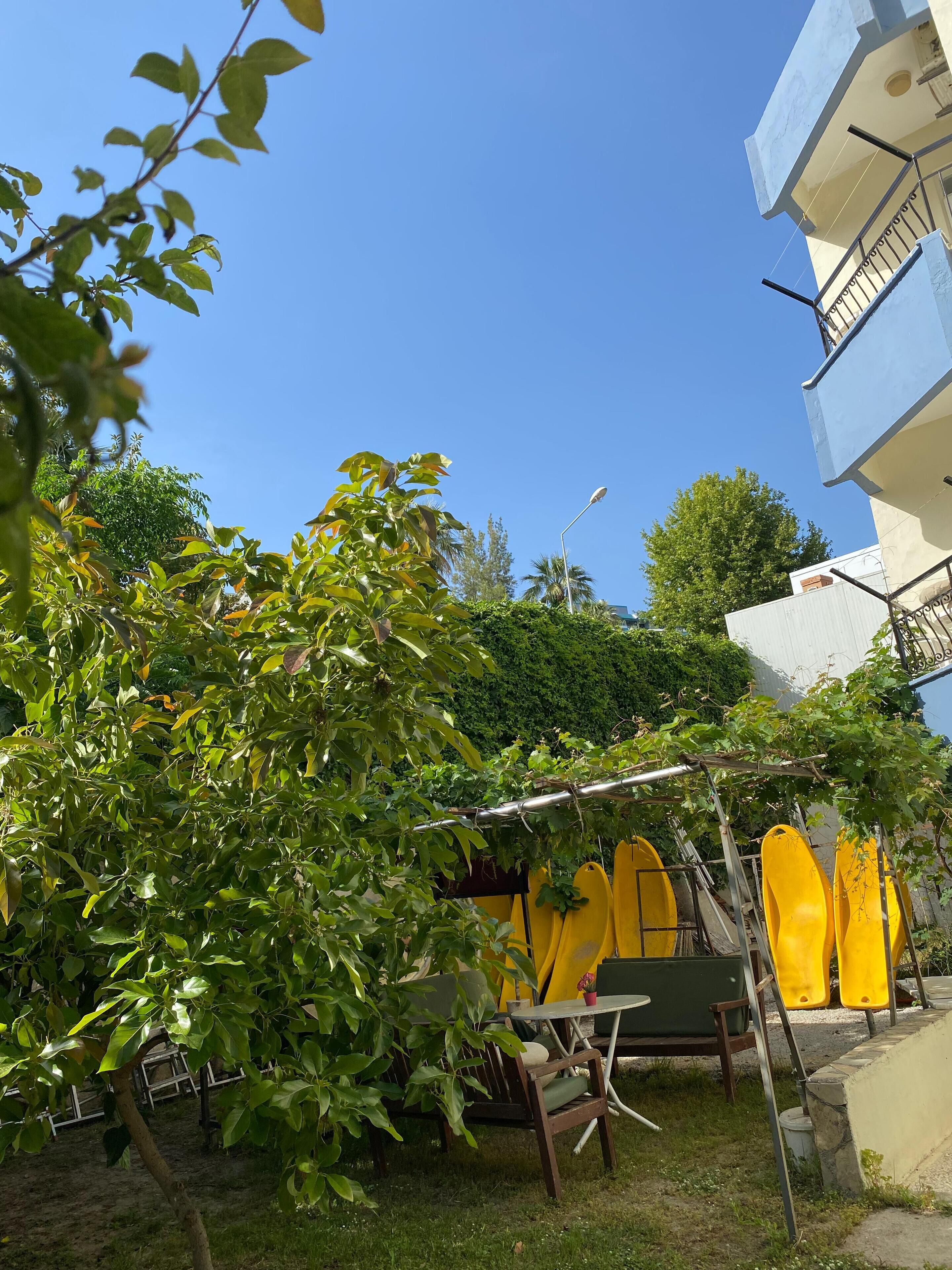 Un patio con una mesa y sillas, rodeado de follaje y un edificio con balcones.