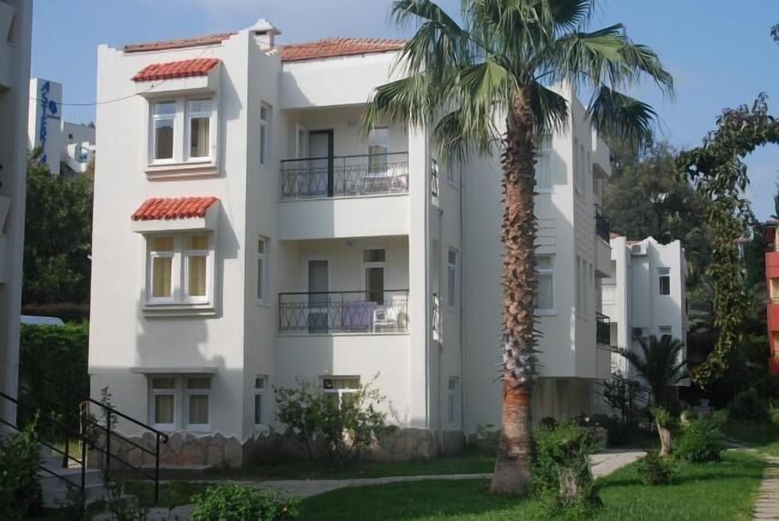A multi-story residential building with balconies, a palm tree, and a well-maintained lawn.