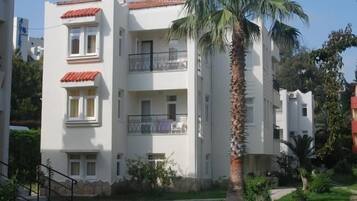 A multi-story residential building with balconies, a palm tree, and a well-maintained lawn.