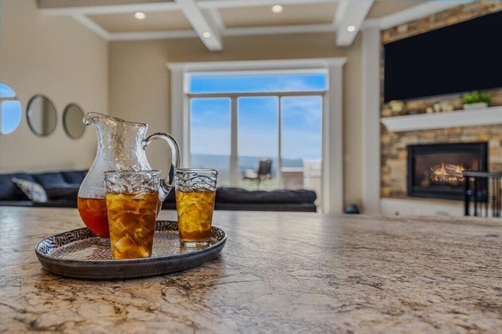 A living room with a fireplace, a large window, and a table with a pitcher and glasses of a beverage.