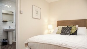 Een slaapkamer met een bed, nachtkastje met lamp, een spiegel aan de muur en een badkamer met wastafel en toilet.