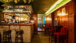 Een bar met krukken, een toonbank vol flessen en uitzicht op de ruimte.
