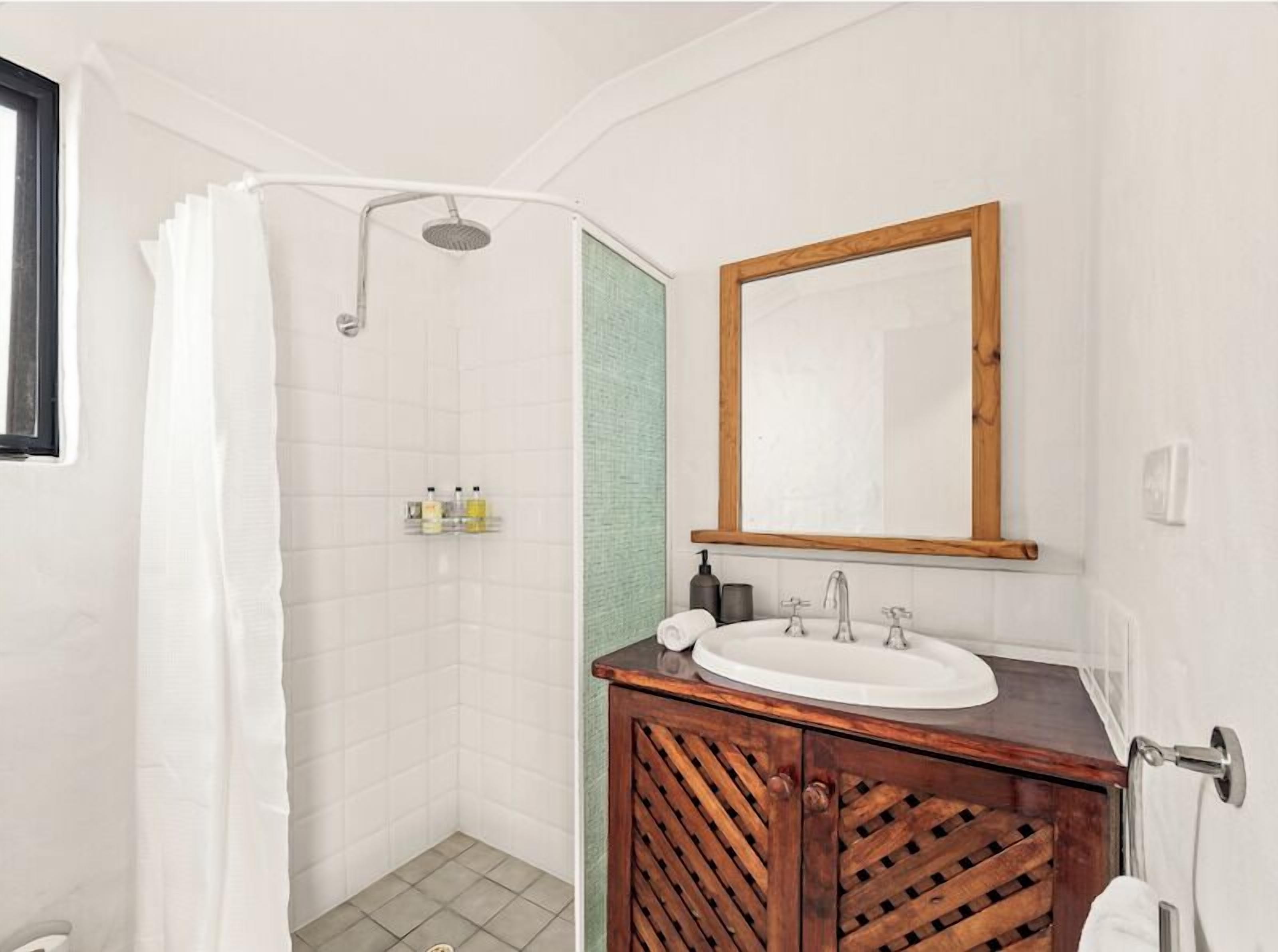 A bathroom with a shower, a sink with a wooden vanity, and a mirror.