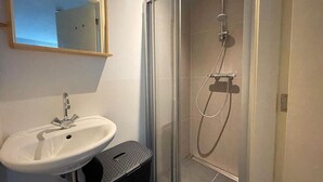 Une salle de bain avec un lavabo blanc, un miroir et une douche séparée par une paroi de verre.