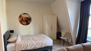 Une chambre à coucher moderne avec un lit, une chaise, une armoire et une œuvre d’art circulaire accrochée au mur.