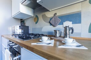 Uma cozinha moderna com fogão a gás, duas chávenas brancas em pires, chaleira e forno de micro-ondas.
