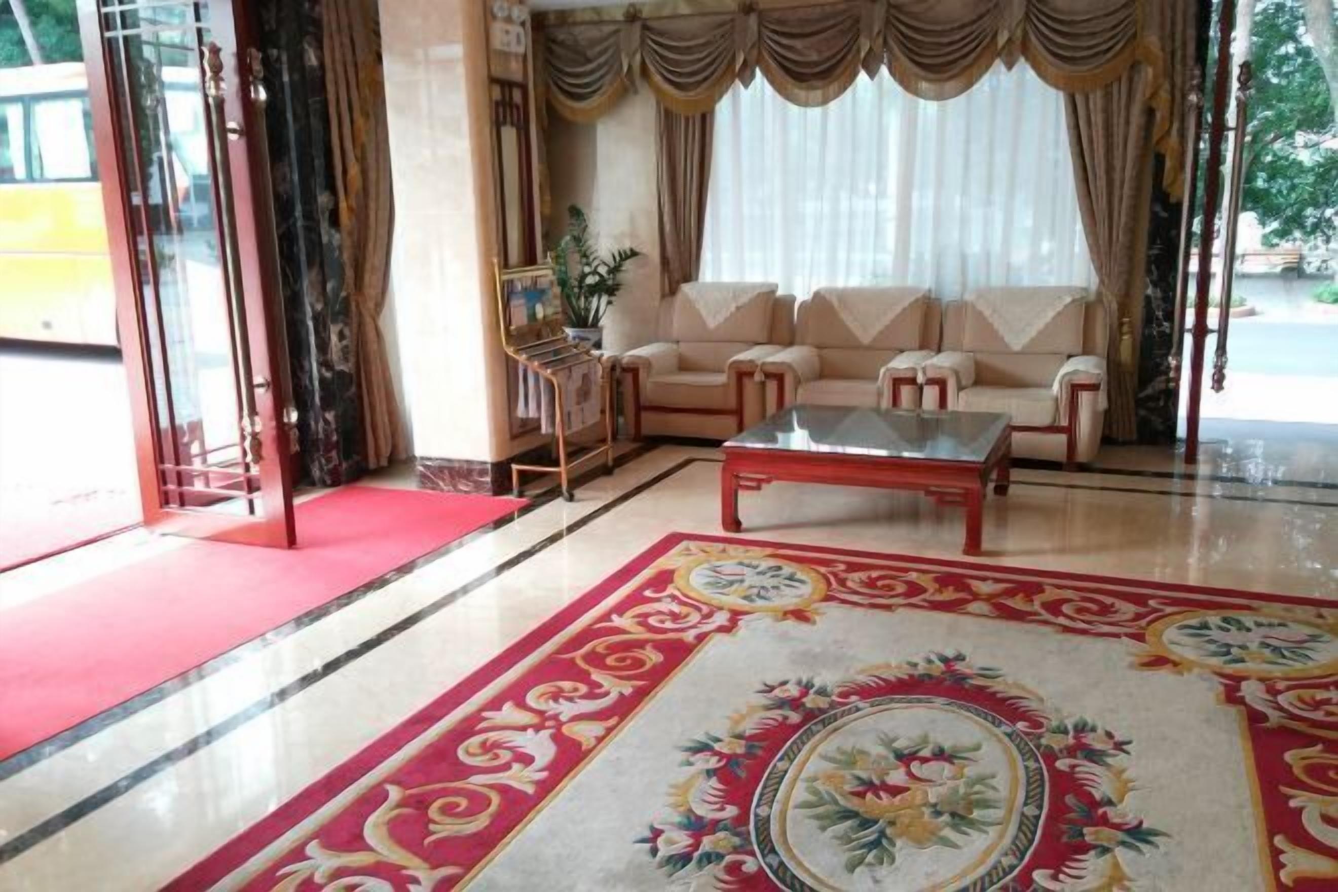 A spacious living room with a red carpet, beige sofas, a glass coffee table, and a decorative rug.