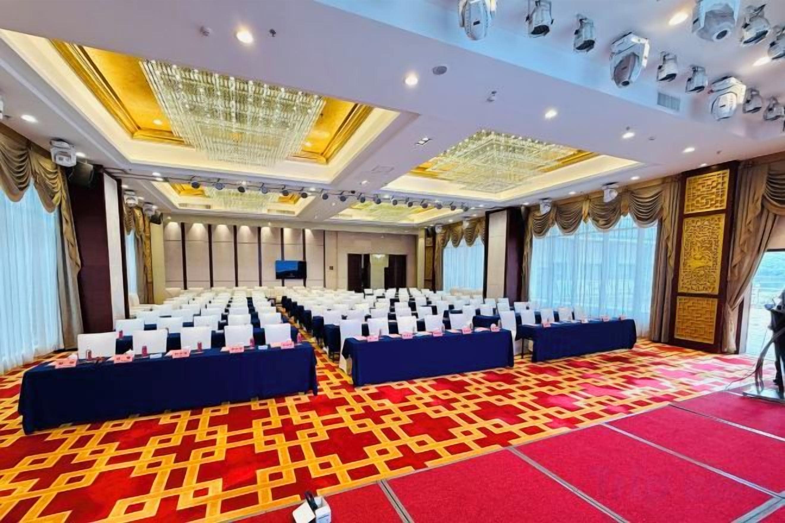 A conference room with rows of chairs, a stage, and a red carpeted floor.