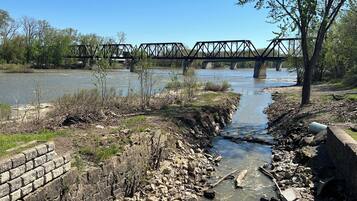 A riverbank with a concrete retaining wall, a metal bridge, and a tree.