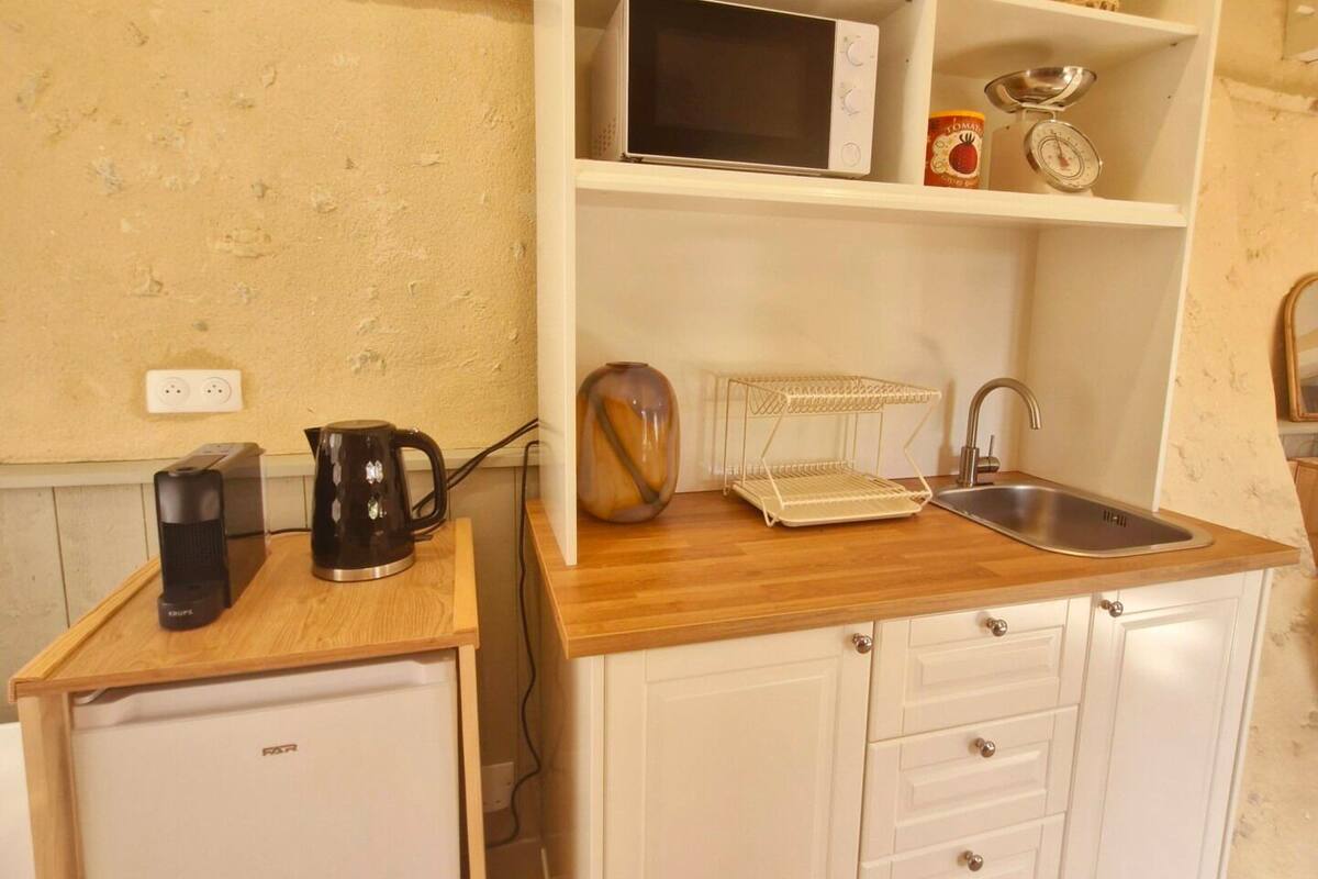 A compact kitchenette with a microwave, kettle, and coffee maker on a wooden countertop, a sink, and a small refrigerator.