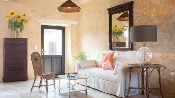 A living room with a white sofa, a wicker chair, a small table, a lamp, a mirror, and a vase with sunflowers. - Casa Pertica  (Ceton)
