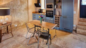 A rustic kitchen with wooden beams, a dining table with chairs, and a modern stove. - Casa Pertica  (Ceton)