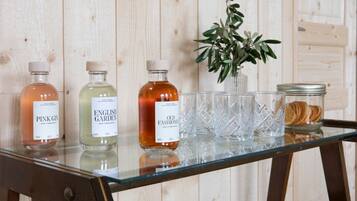 A glass table with three bottles of gin, a vase with green foliage, and a jar of dried orange slices.