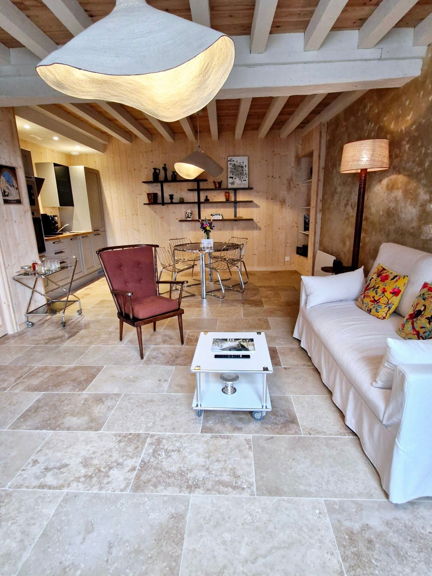 Un vaste espace de vie doté d’un plafond en bois, d’une table à manger avec des chaises, d’un canapé agrémenté de coussins colorés et d’un meuble sur roulettes avec un téléviseur à écran plat.