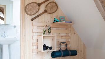 A wooden interior with a sloped ceiling, a wicker basket, shelves with yoga mats, and tennis rackets.