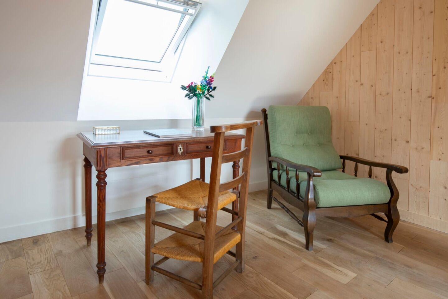 A room with a wooden desk, a green upholstered chair, and a skylight.