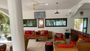 Un espacio interior amplio con mobiliario de mimbre, ventanas grandes y un ventilador de techo.