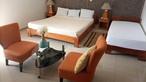 Habitación de hotel con una cama grande, dos sillones, una mesita de vidrio con un florero y dos lámparas de noche.