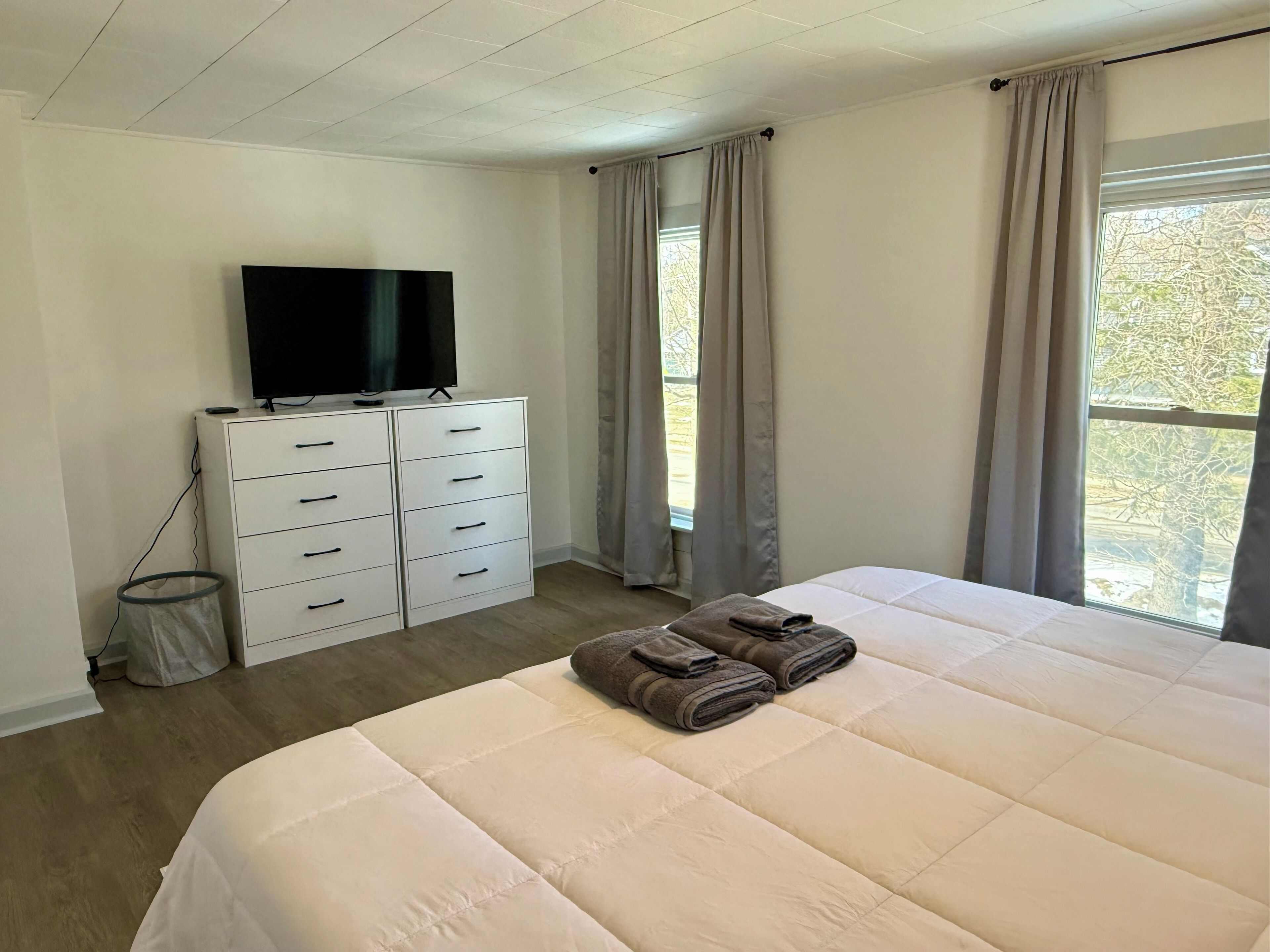 Un dormitorio con una cama grande, un televisor en una cómoda y una ventana con cortinas.