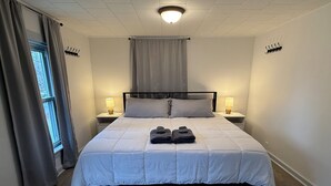 En snyggt bäddad säng med ett vitt täcke, två sänglampor och ett fönster med gardiner.