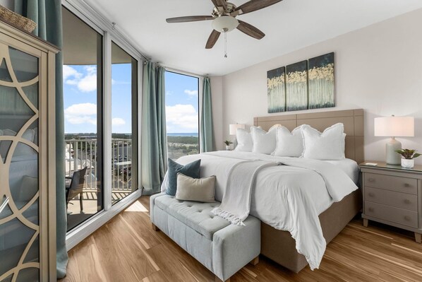 A bedroom with a large bed, a bench, a nightstand, and a view of the outdoors.