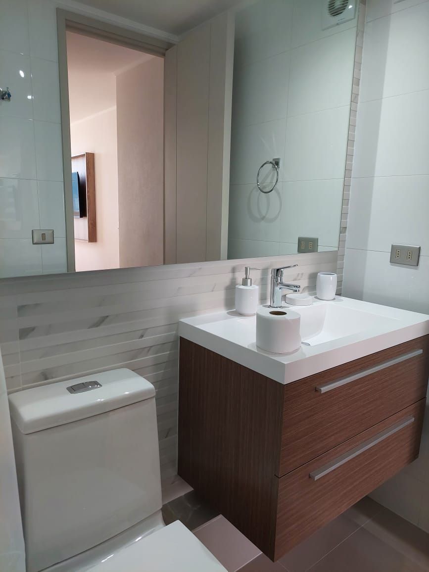 Uma casa de banho moderna com lavatório branco, toucador de madeira e sanita.