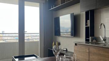 A modern dining area with a wooden table set for four, a hanging light fixture, and a city view through large windows.