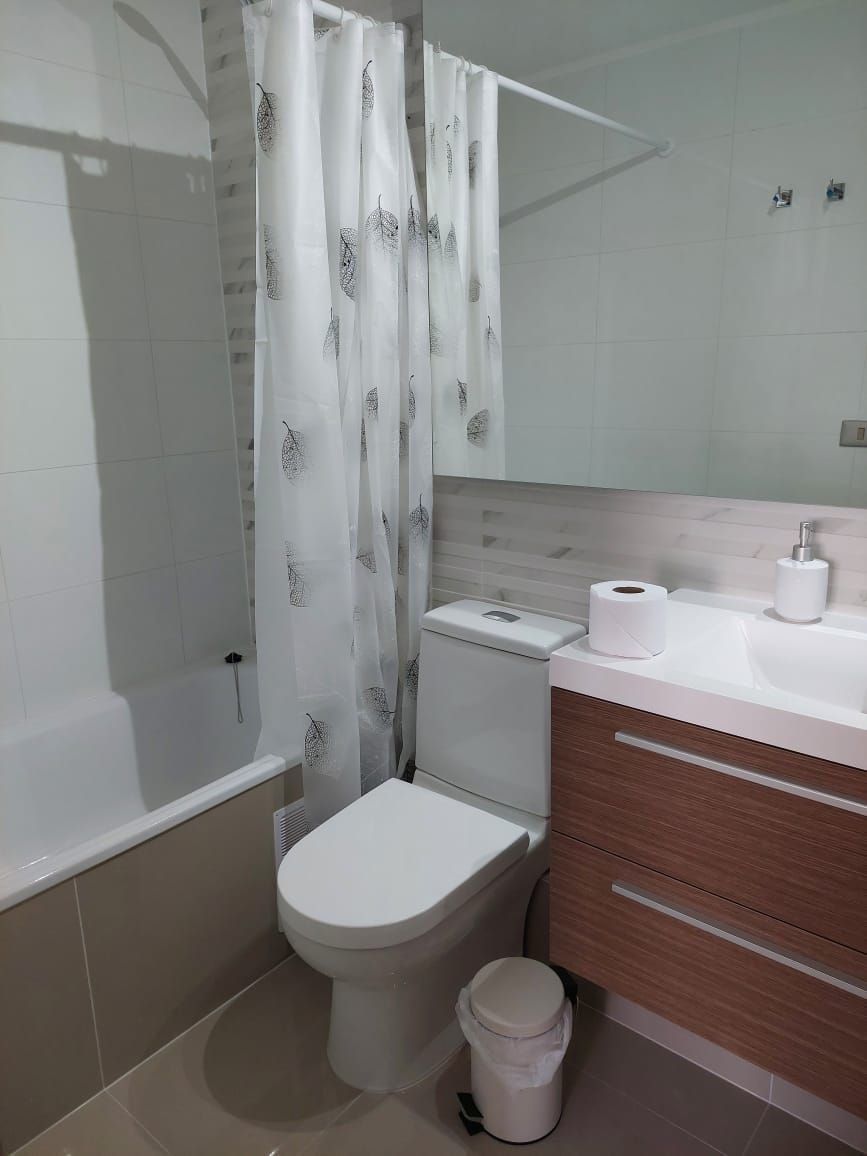 A bathroom with a toilet, a bidet, a shower curtain, a sink with a mirror, and a toilet paper holder.