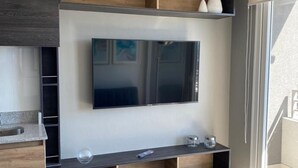 Eine moderne Küche mit integriertem Fernseher, Holzschränken und einem Essbereich mit Barhocker.