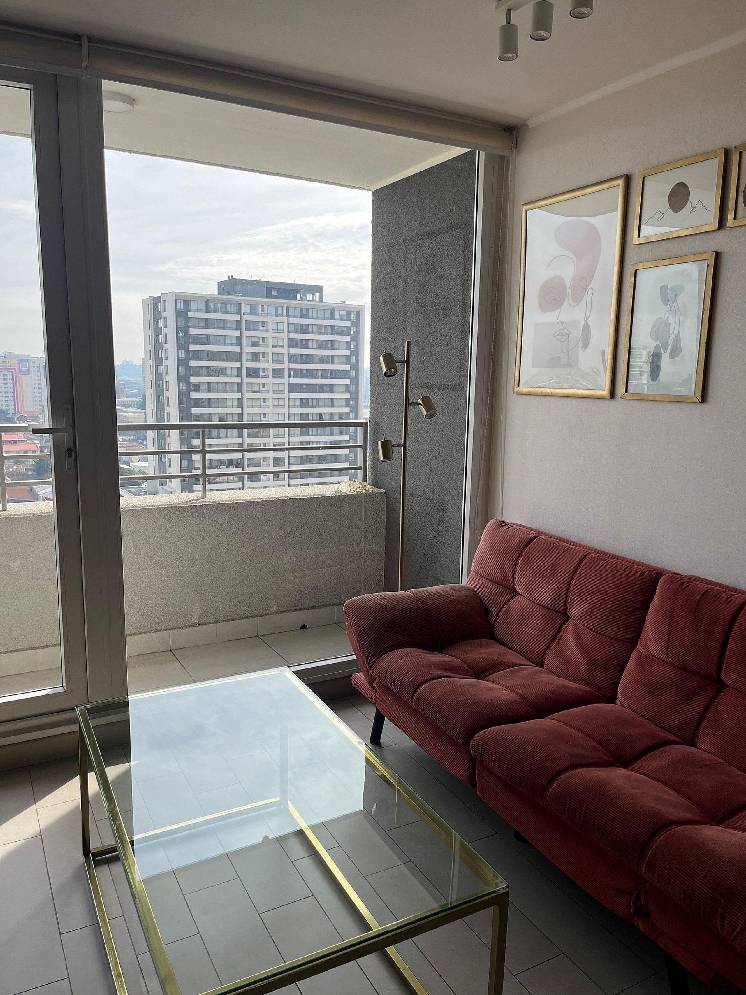 A modern living room with a red sofa, a glass coffee table, and a city view through large windows.