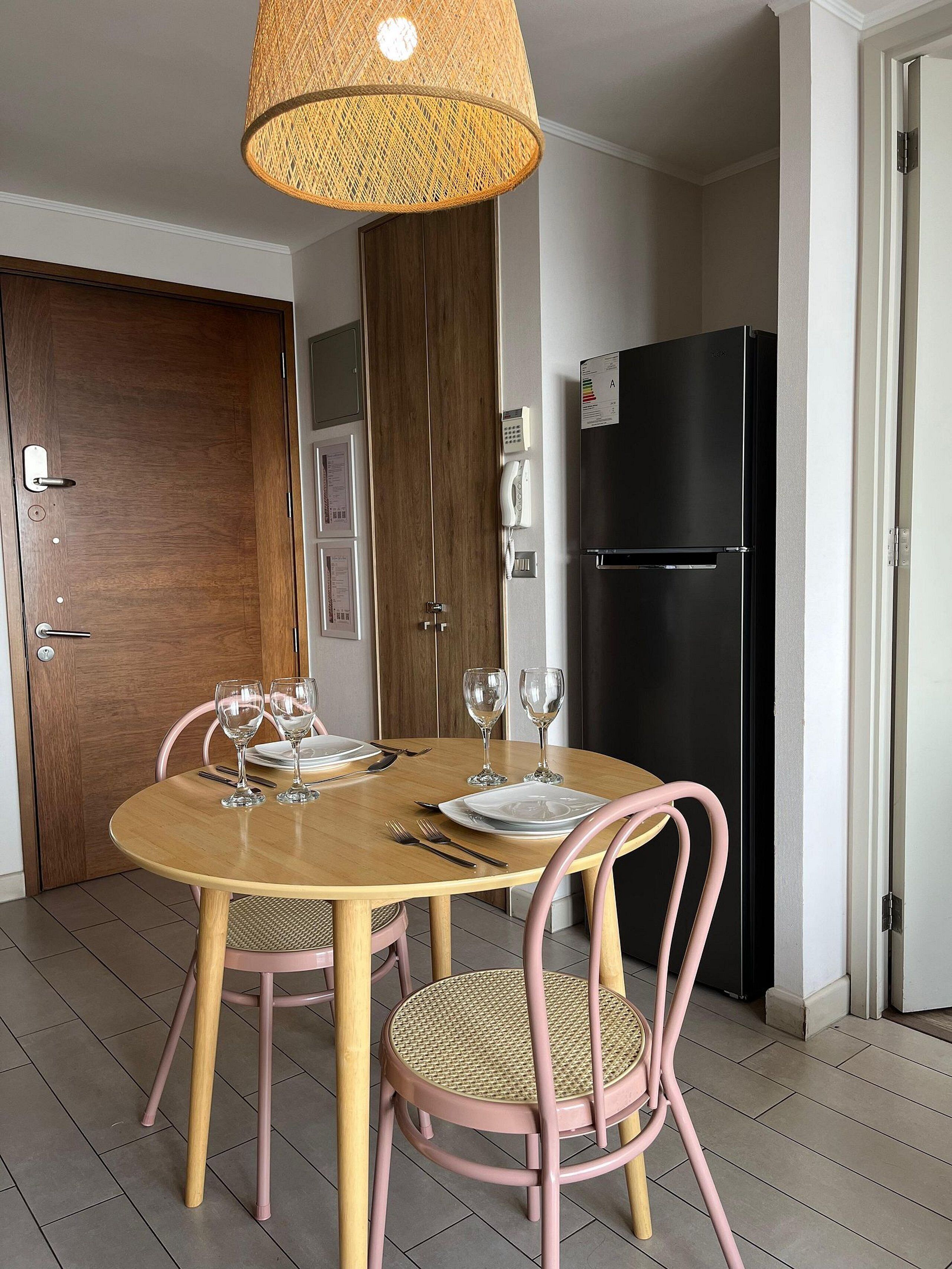 Un comedor con una mesa redonda, sillas rosadas y un refrigerador negro.