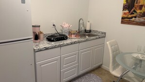 Una cocina compacta con refrigerador, lavamanos doble y una mesa de vidrio con sillas.