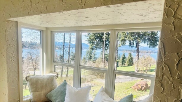 A cozy room with a large bay window overlooking a lake and trees.