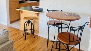 A compact kitchen with wooden cabinets, a central island, and a dining area with metal chairs and stools.