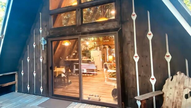 Une terrasse en bois avec une grande porte vitrée donnant sur un espace intérieur, le tout entouré d’arbres.