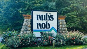 Une pancarte portant l’inscription « hub’s nob », entourée d’un mur de pierres et d’une végétation luxuriante.