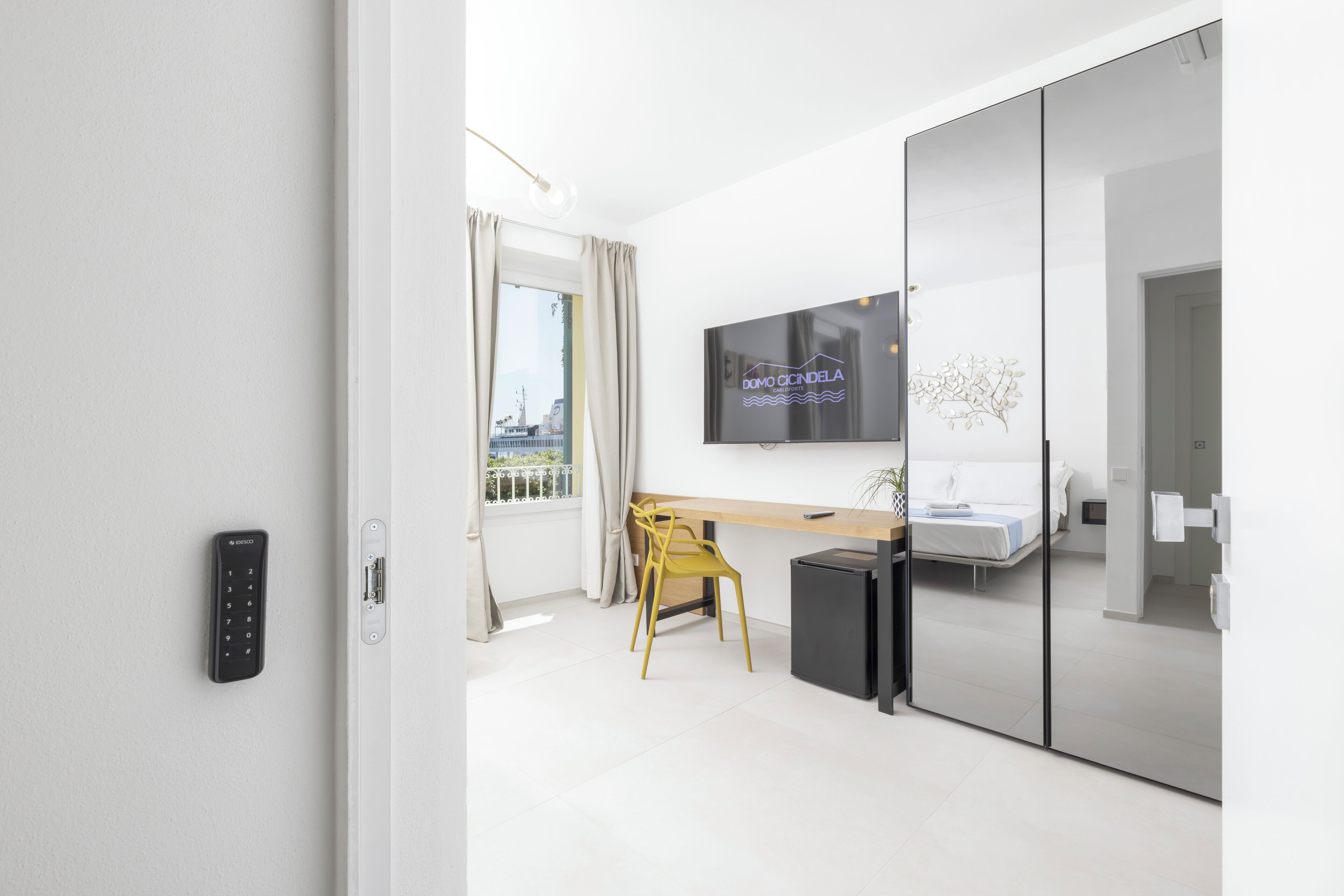 Una moderna camera d'hotel con porta scorrevole, un letto, una scrivania, una sedia, una TV e vista sulla città.