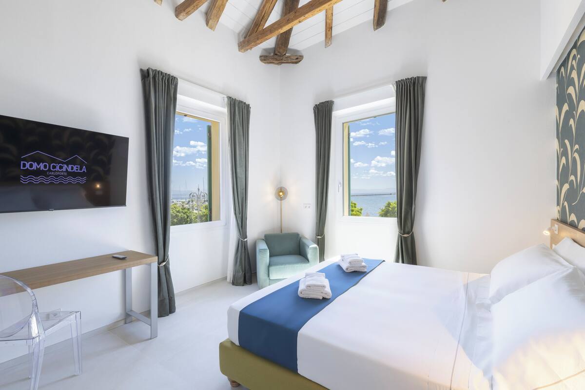 A modern hotel room with a bed, a desk, a chair, and a TV mounted on the wall.