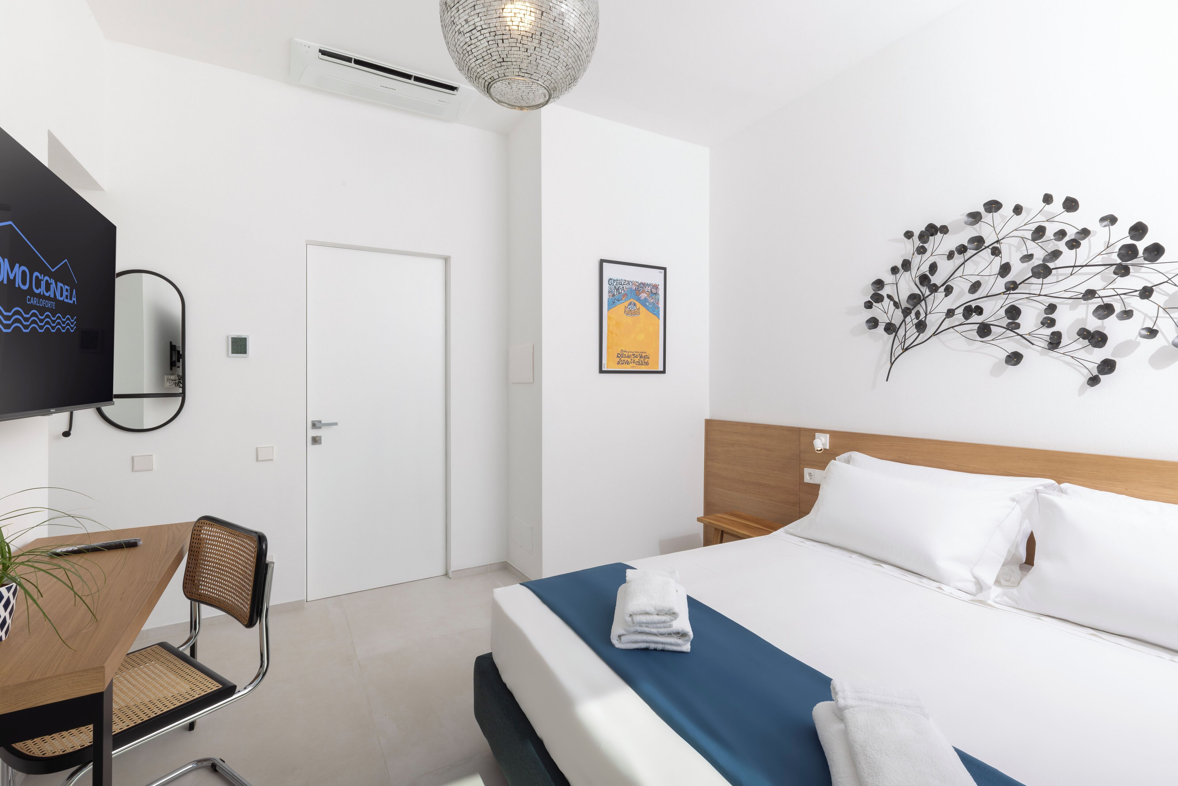 A hotel room with a bed, a desk with a chair, a television, and a wall art piece.