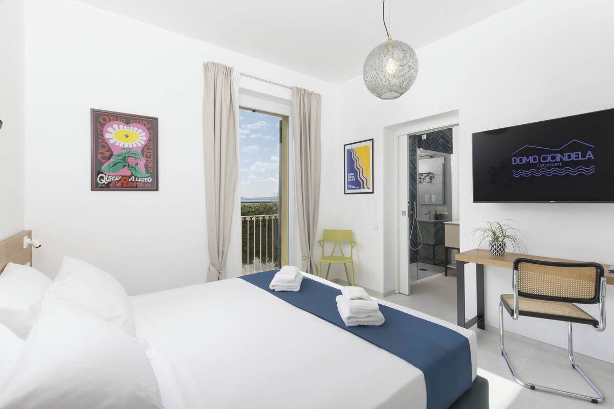 A hotel room with a bed, a desk, a chair, a TV, and a balcony.