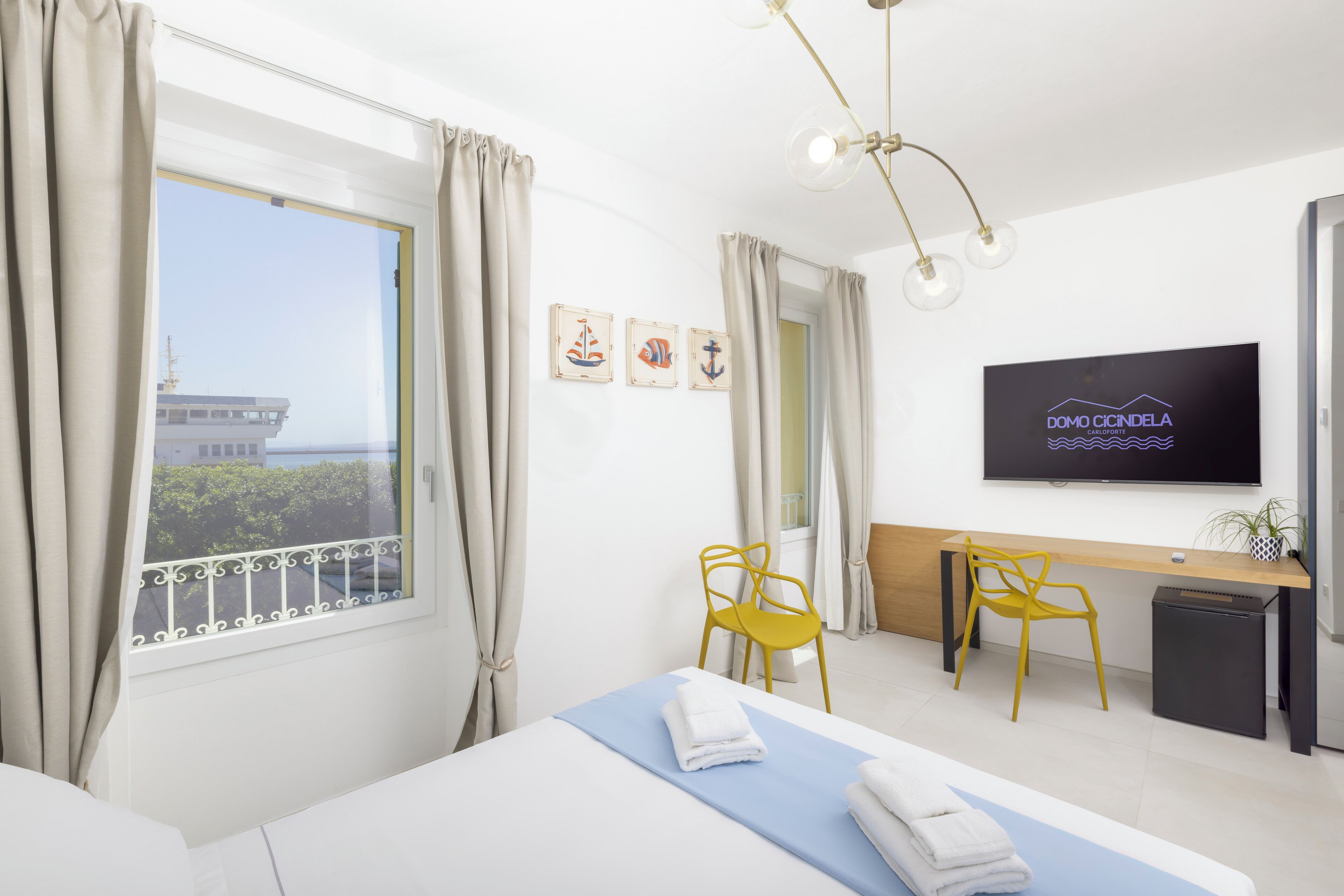Hotelkamer met een bed, een bureau, twee gele stoelen, een televisie en een raam met gordijnen.