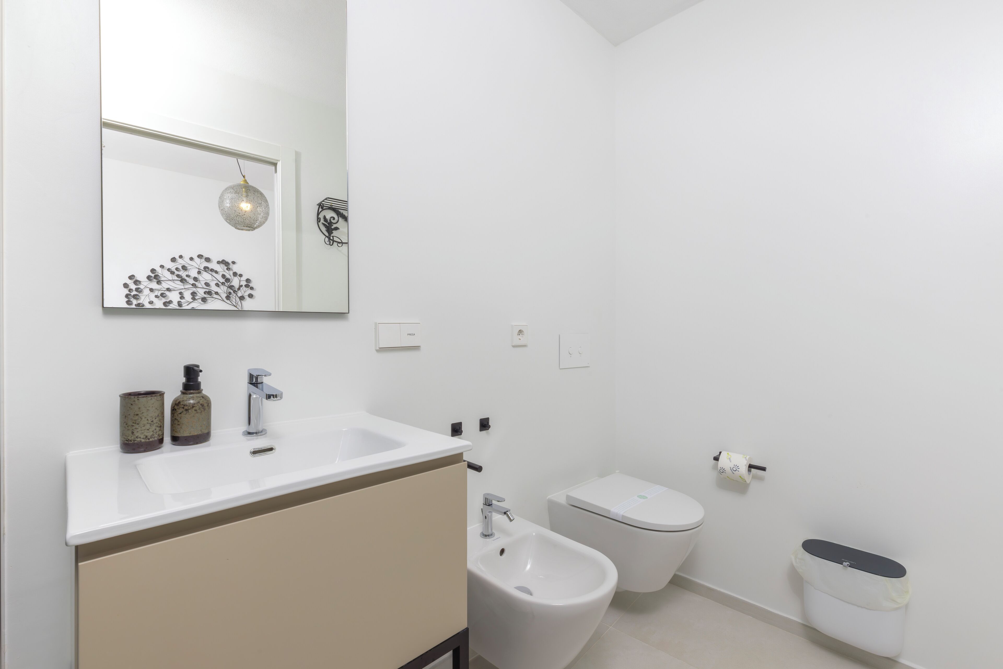 Une salle de bain moderne avec un lavabo blanc, un bidet, des toilettes et une poubelle.