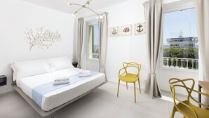A modern hotel room with a bed, a yellow chair, and a view of a building through the window. - DOMO CICINDELA (Carloforte)