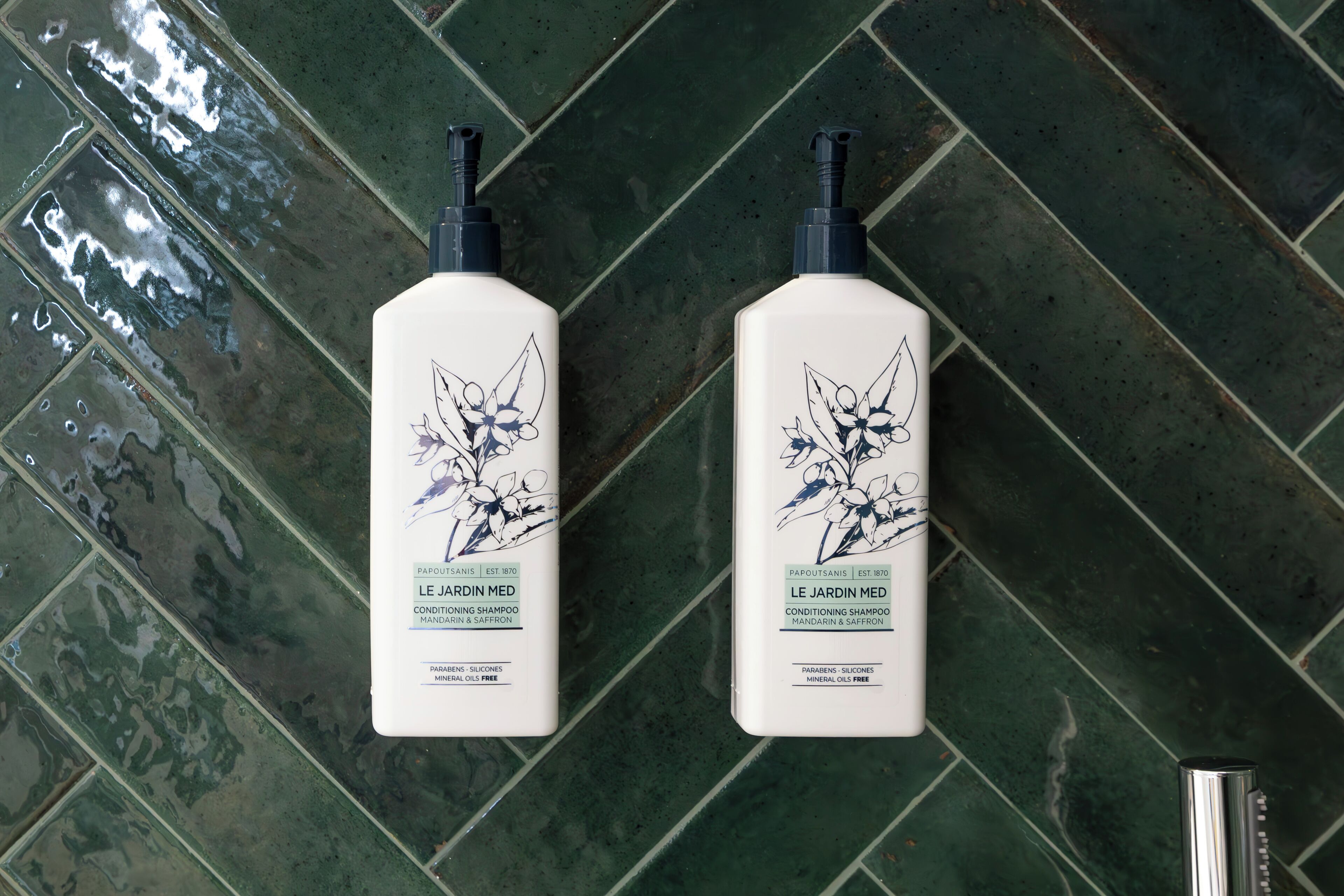 Two bottles of Le Jardin Med conditioning shampoo on a green tiled floor.